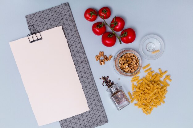 Vista de ángulo alto del ingrediente de pasta con papel blanco en blanco y servilleta sobre superficie gris