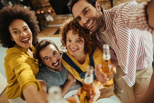 Vista de ángulo alto de jóvenes felices divirtiéndose mientras toman selfie y beben cerveza en casa
