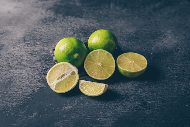 Foto gratuita vista de ángulo alto limones verdes con rodajas sobre fondo negro con textura. horizontal