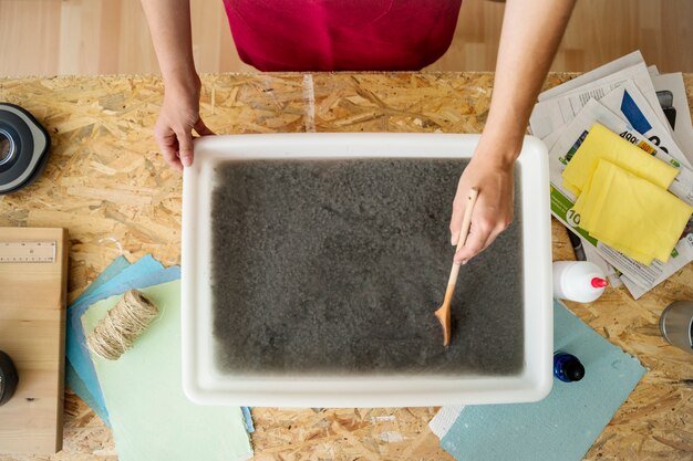 Vista de ángulo alto de la mano de una mujer que remueve la pulpa de papel en la bandeja