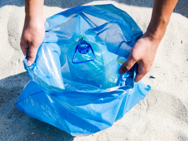 Foto gratuita vista de ángulo alto de manos sosteniendo una bolsa de basura azul en la arena