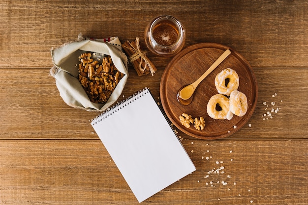 Vista de ángulo alto de la miel; rosquilla; nuez; bloc de notas de canela y espiral en escritorio de madera