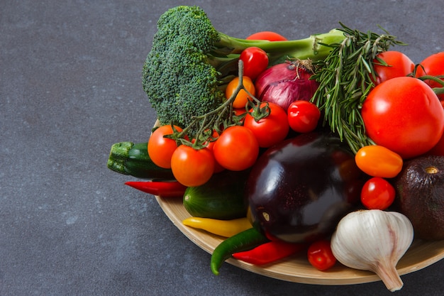 Vista de ángulo alto un montón de tomates con pimientos, cebolla, berenjena, verduras, brócoli, ajo en superficie gris. horizontal