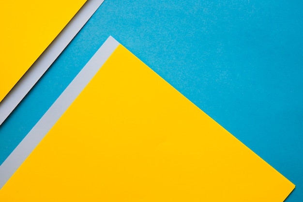 Vista de ángulo alto de papeles de cartón amarillos y grises sobre fondo azul