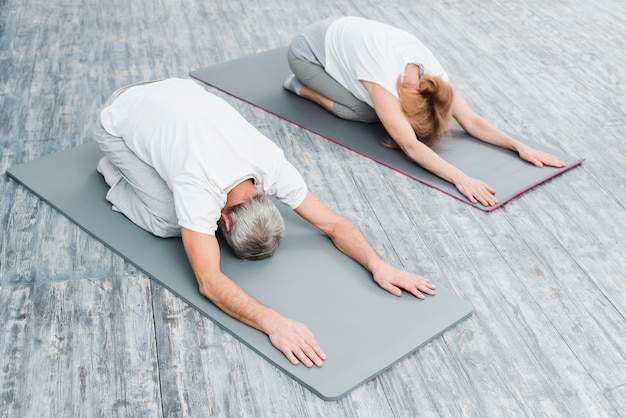 Foto gratuita vista de ángulo alto de una pareja en el equipo blanco que practica estirando posiciones de yoga