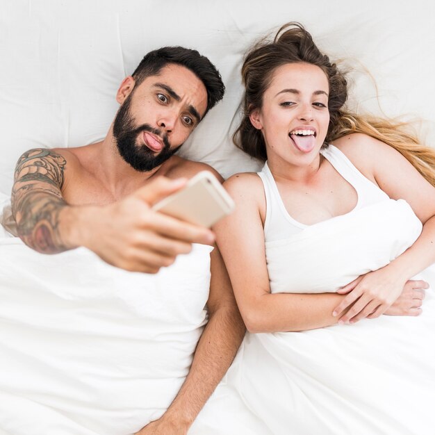 Vista de ángulo alto de una pareja sacando la lengua mientras toma autofoto en un teléfono inteligente