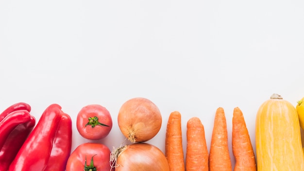 Vista de ángulo alto de pimiento rojo; los tomates cebollas; Zanahorias y calabaza en superficie blanca