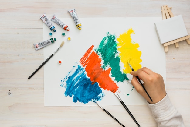 Vista de ángulo alto de pintura de mano humana sobre papel blanco con pincelada colorida