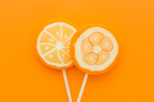 Vista de ángulo alto de piruletas dulces frescas de cítricos en superficie naranja