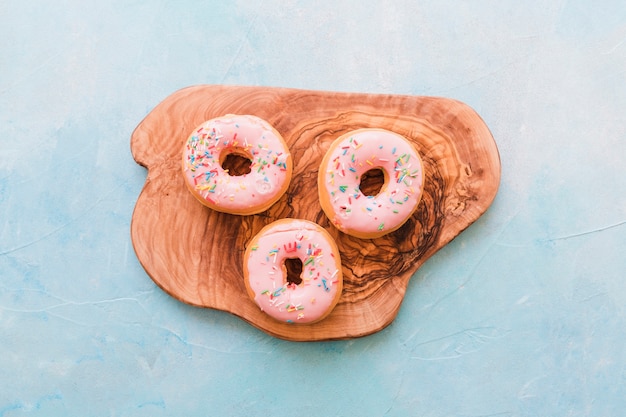 Vista de ángulo alto de rosquillas rosadas en tabla de cortar de madera