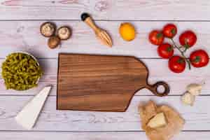 Foto gratuita vista de ángulo alto de la tabla de cortar de madera que rodea la pasta cruda y el ingrediente en la mesa