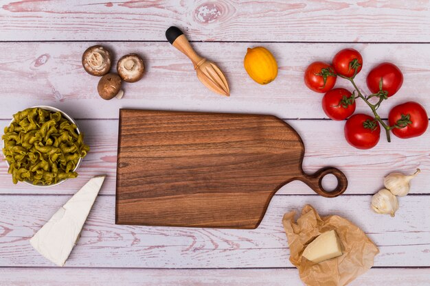 Vista de ángulo alto de la tabla de cortar de madera que rodea la pasta cruda y el ingrediente en la mesa