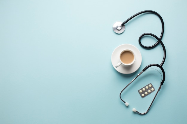 Vista de ángulo alto de la taza de café; Estetoscopio y medicina en blister sobre fondo azul