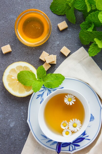 Vista de ángulo alto una taza de té de manzanilla con azúcar, hojas, miel, limón.