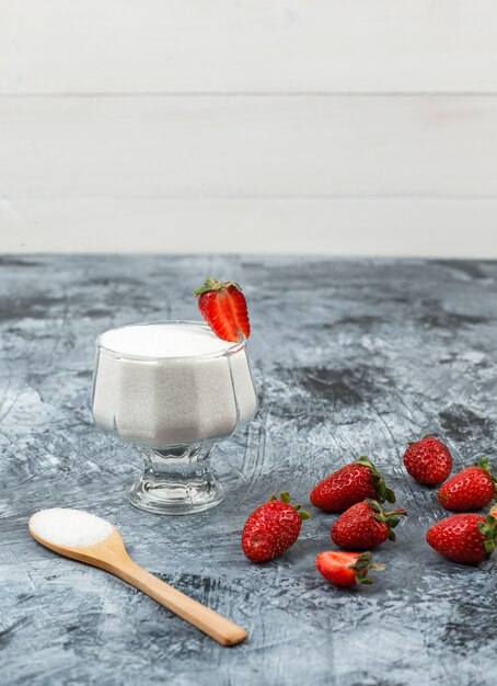 Vista de ángulo alto un tazón de vidrio de yogur en mantel de mimbre con cuchara de madera y fresas sobre fondo de tablero de madera blanca y mármol azul oscuro. espacio libre vertical para su texto