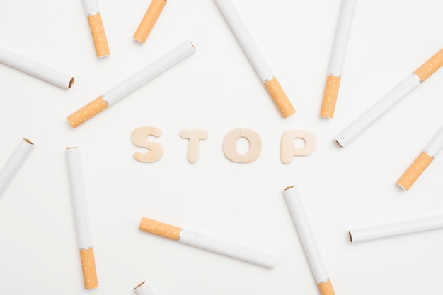 Vista de ángulo alto de texto de parada y cigarrillos sobre fondo blanco