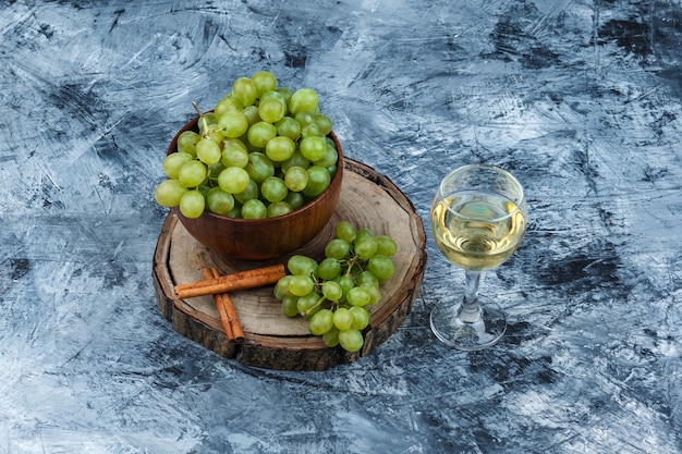 Foto gratuita vista de ángulo alto de uvas blancas, canela sobre tabla de madera con vaso de whisky sobre fondo de mármol azul oscuro. horizontal