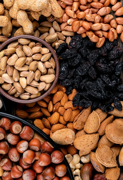 Vista de ángulo alto una variedad de frutos secos y frutas secas en diferentes cuencos con nueces, pistachos, almendras, maní, anacardos, piñones. vertical