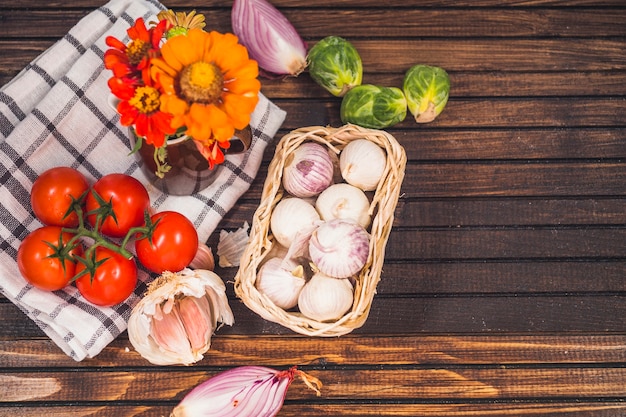 Foto gratuita vista de ángulo alto de vegetales crudos en ingredientes con flores y tela sobre fondo de madera