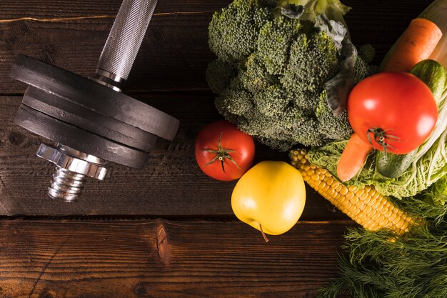 Vista de ángulo alto de vegetales crudos y pesas sobre fondo de madera