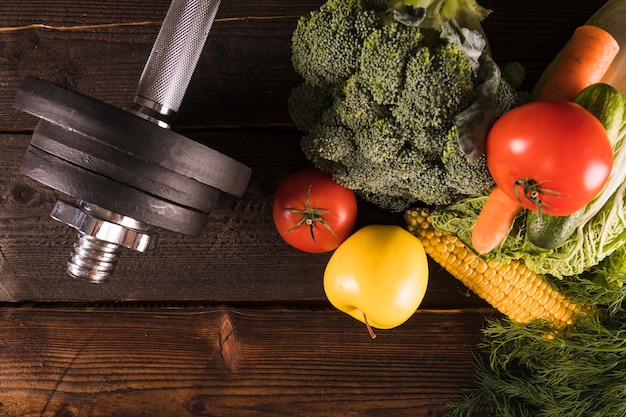 Vista de ángulo alto de vegetales crudos y pesas sobre fondo de madera