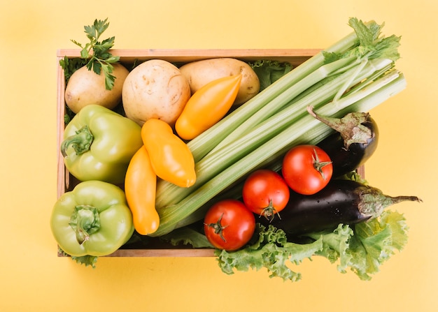 Vista de ángulo alto de verduras frescas en un recipiente sobre fondo amarillo