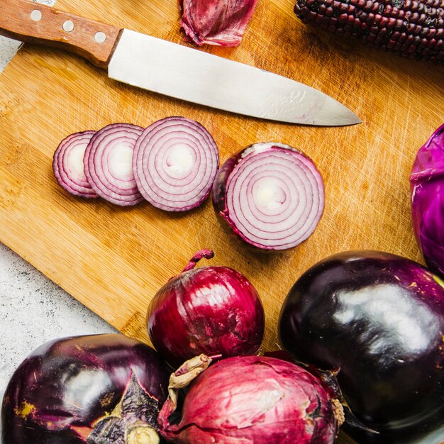 Vista de ángulo alto de verduras; Rodajas de cebolla y cuchillo en tabla de madera para picar