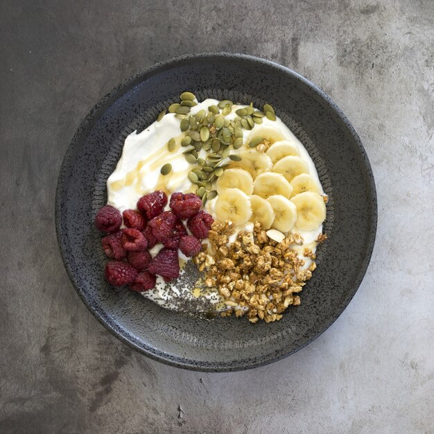 Vista de ángulo alto de yogur con nueces, frambuesas y plátano en un recipiente sobre la mesa