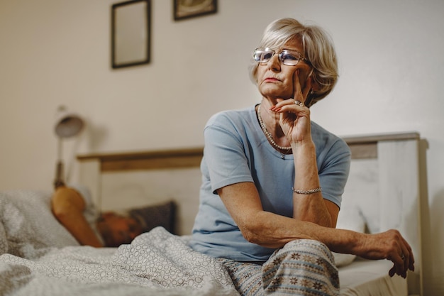 Vista de ángulo bajo de una anciana pensativa que se siente insomne y piensa en algo mientras está sentada en la cama