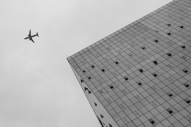 Vista de ángulo bajo a un edificio y un avión volando cerca de él en el cielo