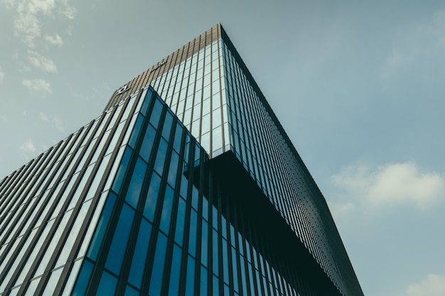 Foto gratuita vista de ángulo bajo de un edificio en una fachada de vidrio bajo el hermoso cielo nublado