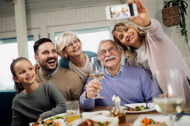 Foto gratuita vista de ángulo bajo de la feliz familia extendida divirtiéndose mientras toma selfie después del almuerzo en la mesa del comedor