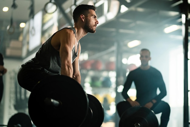 Vista de ángulo bajo del hombre musculoso haciendo peso muerto mientras hace ejercicio con barra en un gimnasio