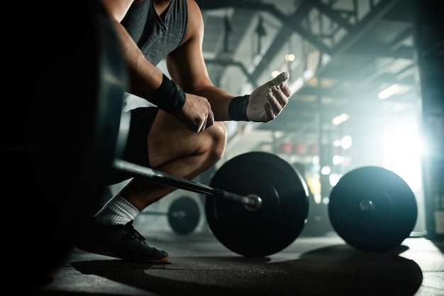 Vista de ángulo bajo del hombre musculoso irreconocible preparándose para levantar una barra en un club de salud