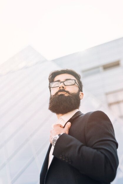 Vista de ángulo bajo del joven empresario de pie contra el edificio corporativo