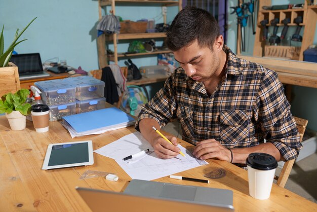 Vista en ángulo del joven fabricante dibujando bocetos en su taller