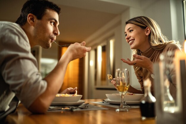 Vista de ángulo bajo de la joven pareja feliz cenando y hablando entre ellos en el comedor