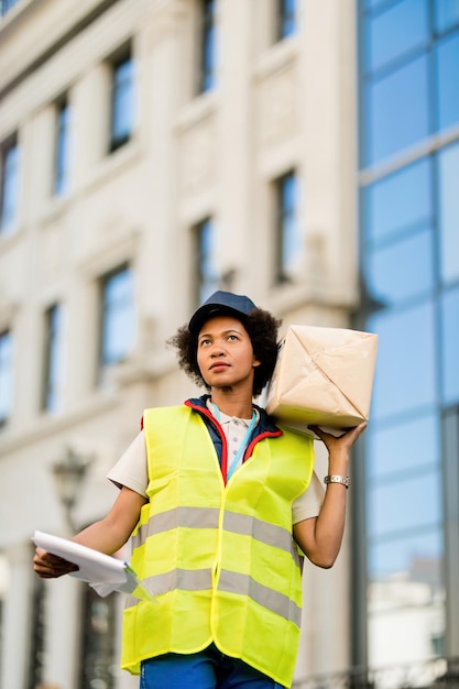 Vista de ángulo bajo del mensajero femenino negro que lleva un paquete de entrega en la ciudad