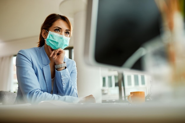 Vista de ángulo bajo de mujer de negocios con máscara facial trabajando en PC de escritorio en la oficina