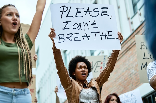 Vista de ángulo bajo de una mujer negra sosteniendo una pancarta con la inscripción No puedo respirar mientras se manifiesta por los derechos humanos con una multitud de personas