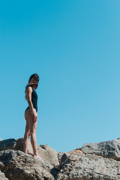 Vista de ángulo bajo de mujer en traje de baño de pie sobre la roca contra el cielo azul