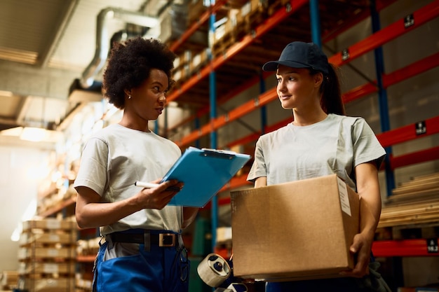 Vista de ángulo bajo de las trabajadoras que se comunican mientras preparan paquetes para una entrega en el almacén de distribución