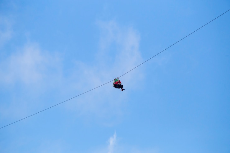 Foto gratuito vista de ángulo bajo de turista montando una aventura de tirolesa contra el cielo azul