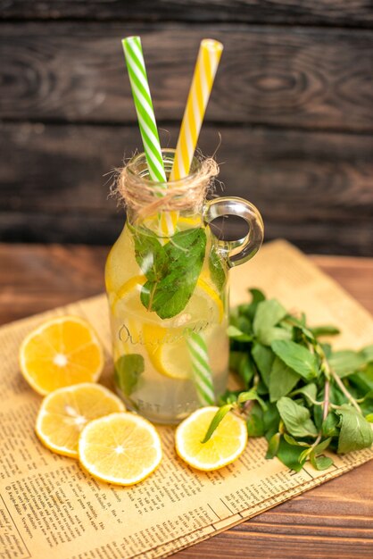 Vista anterior de agua de desintoxicación hecha de limón y menta en un periódico viejo sobre fondo de madera marrón