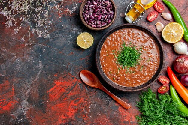 Vista anterior de la botella de aceite de sopa de tomate frijoles limón y un montón de verde en la tabla de colores mezclados