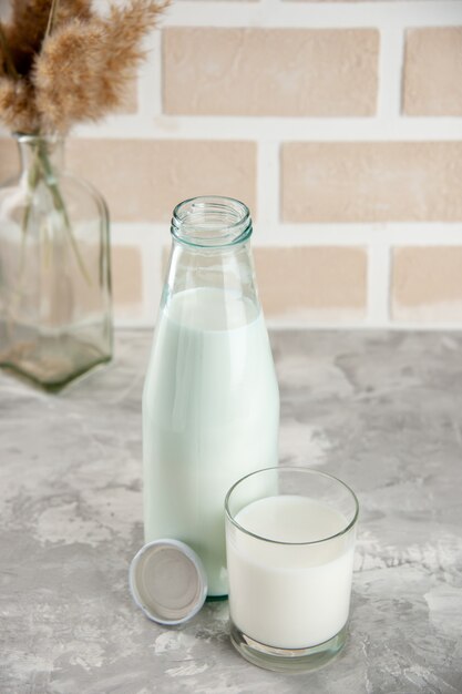 Vista anterior de la botella de vidrio y la taza llena con tapón de leche sobre fondo de ladrillo de color pastel