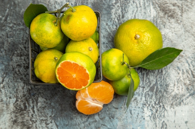 Vista anterior de una canasta con mandarinas verdes frescas cortadas por la mitad y mandarina pelada sobre fondo gris