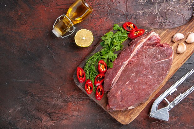 Vista anterior de la carne roja en la tabla de cortar de madera y ajo verde pimiento picado botella de aceite caído limón sobre fondo oscuro