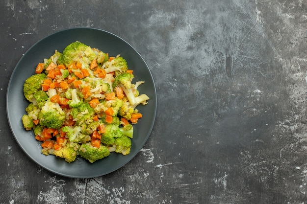 Vista anterior de comida saludable con brocoli y zanahorias en una placa negra sobre tabla gris