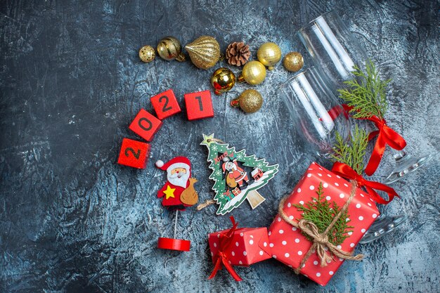 Vista anterior de copas de vidrio caídas y cubiertos, accesorios de decoración, caja de regalo y números de calcetines de navidad en el cuadro oscuro